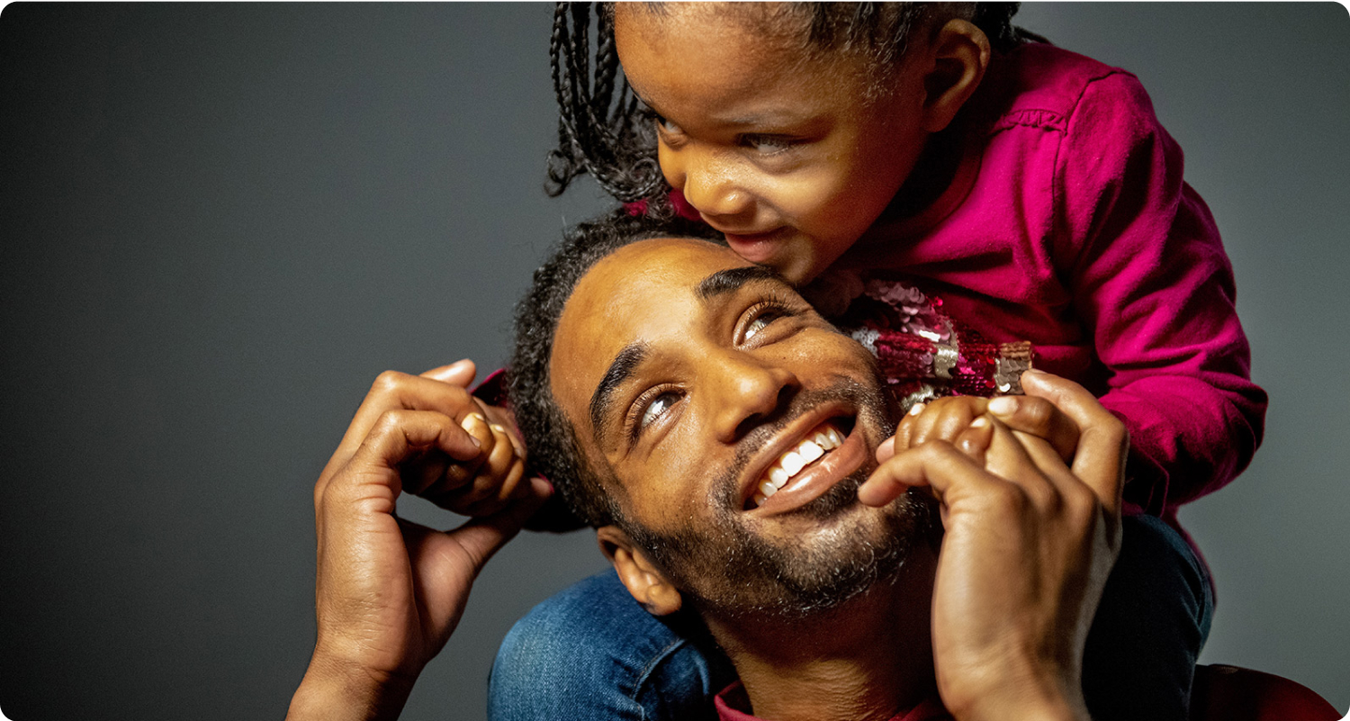 African American father and daughter, with daughter on shoulders and both happy